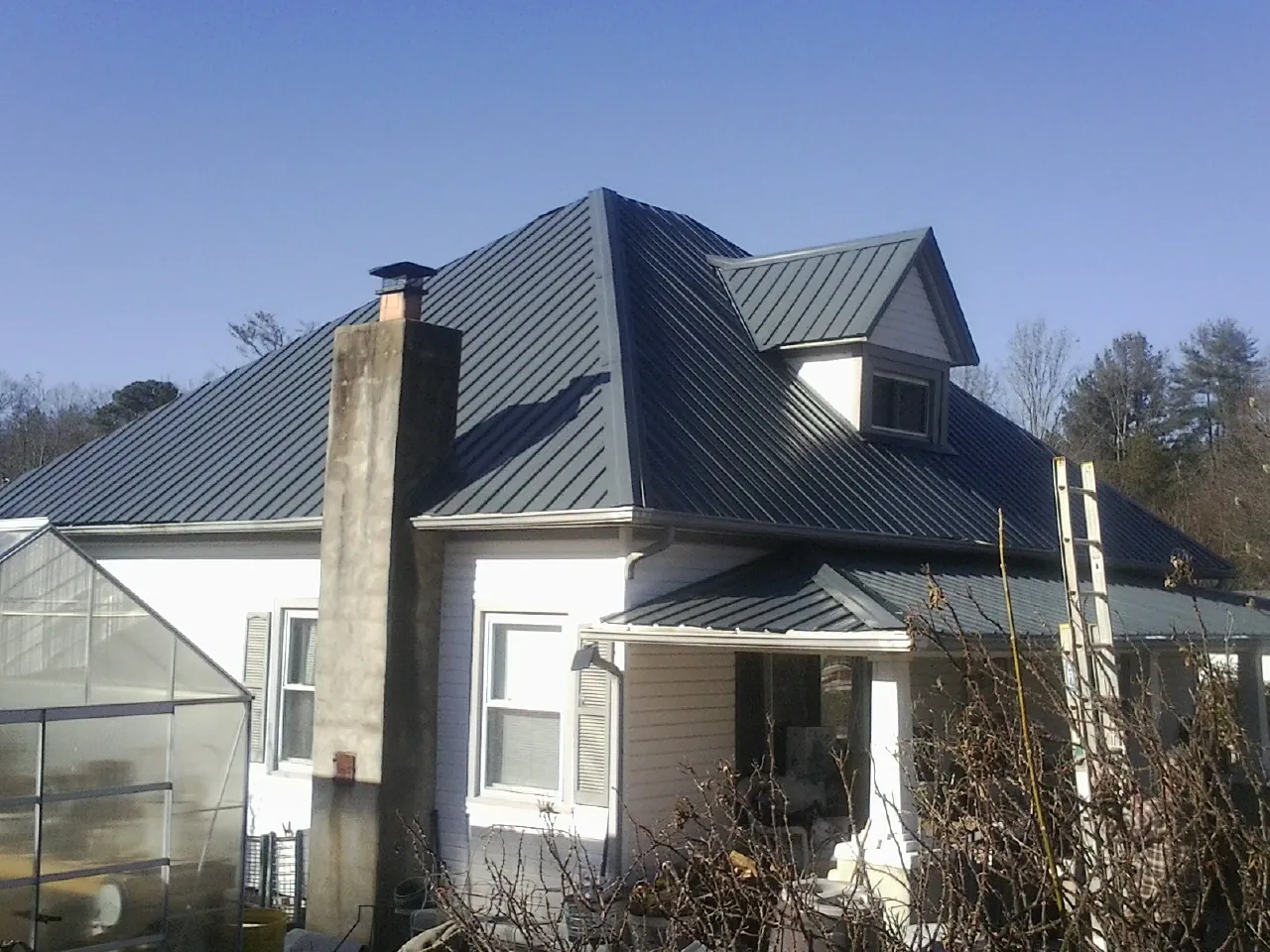 Dark blue standing seam metal roof on a white farmhouse with dormer — Slate & Tile Roof Repair by Roofing Brothers in Rosemead